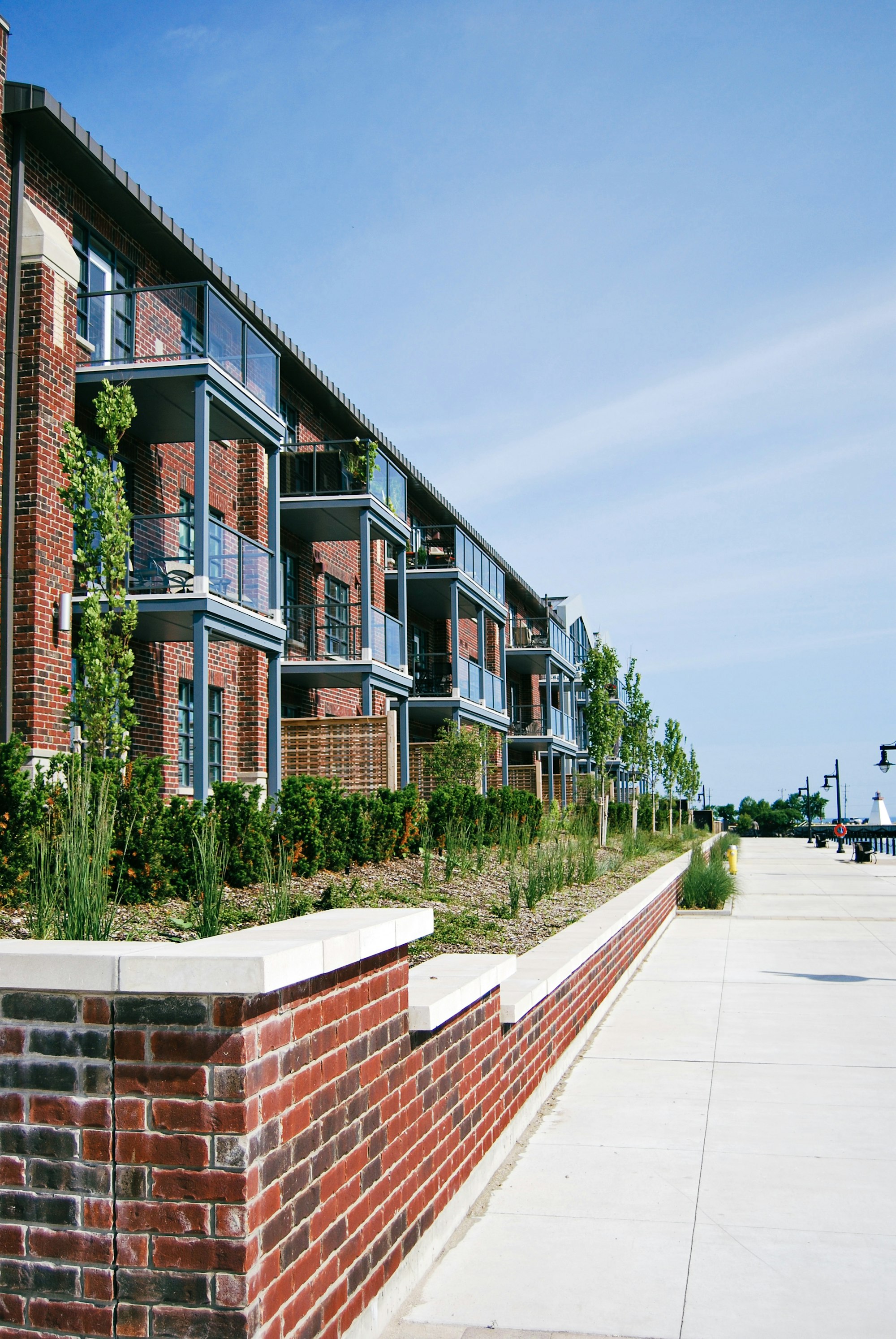 A red brick apartment building with glass balconies along a waterfront walkway