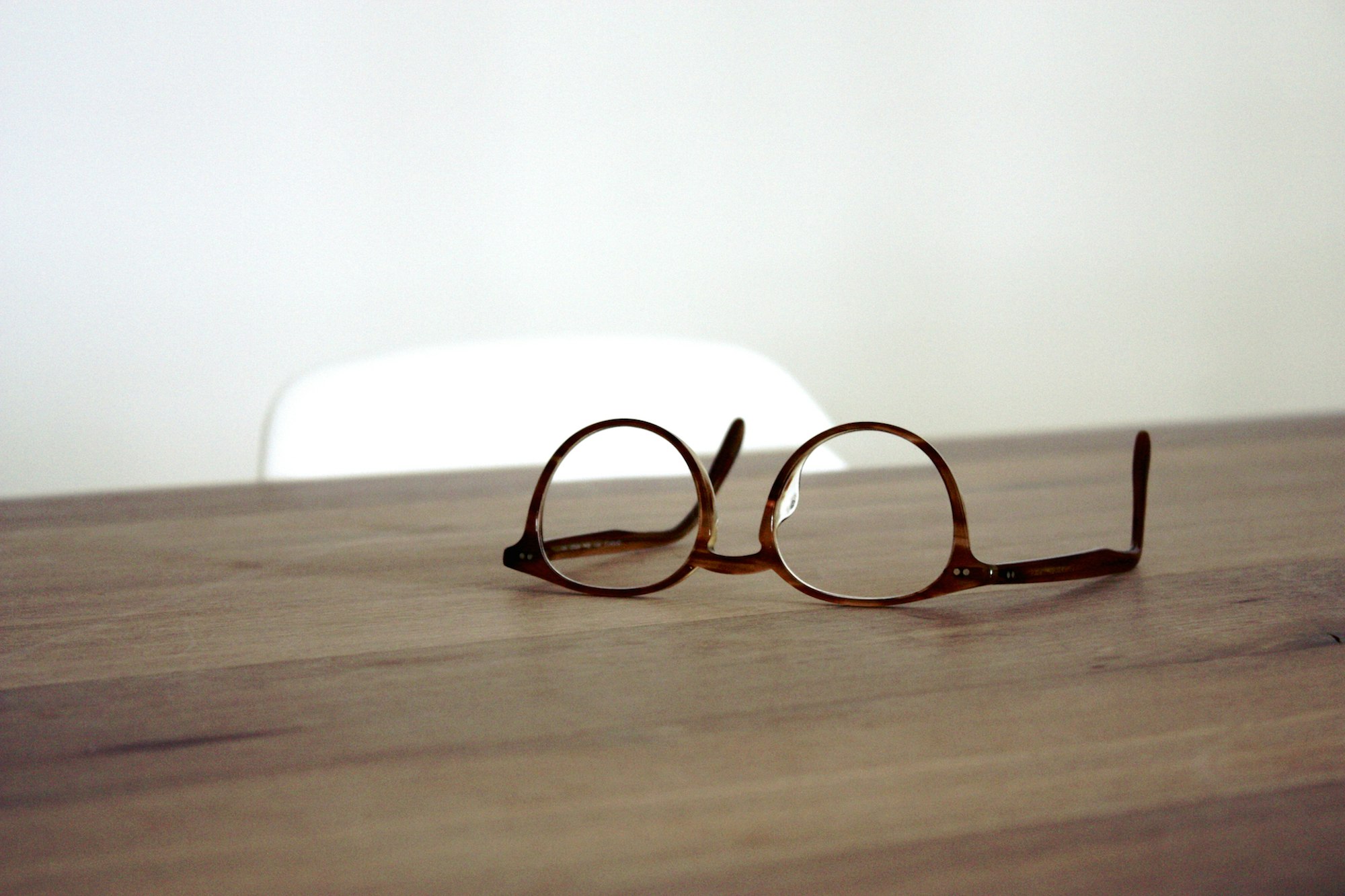 A pair of round tortoiseshell eyeglasses resting on a wooden table