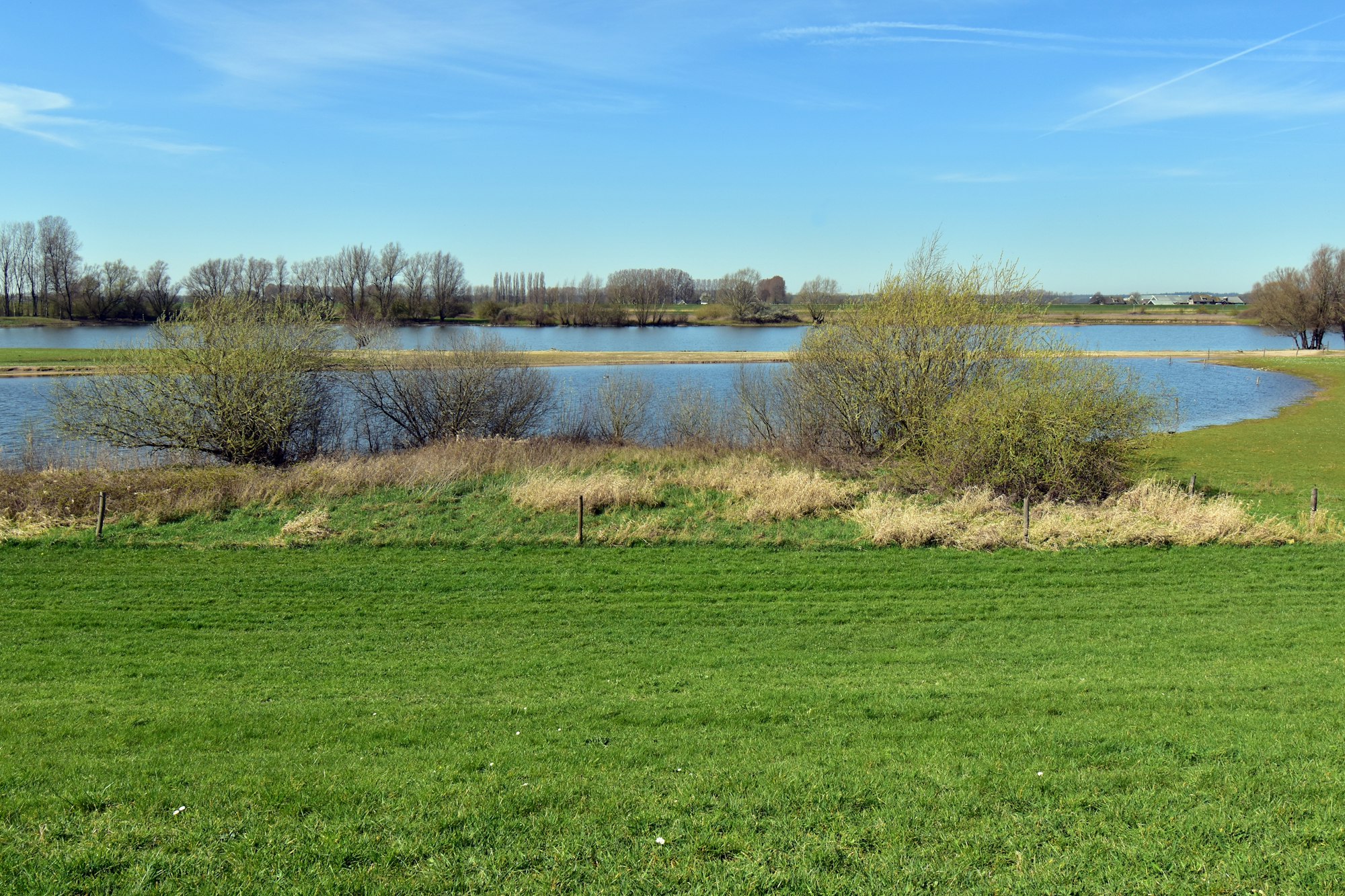 A flooded riverside field and lake under a clear blue sky