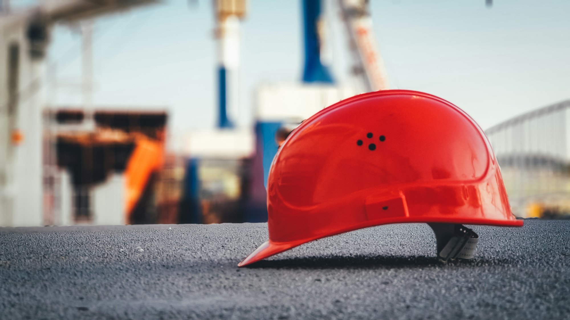 A red safety hard hat resting on a construction site surface