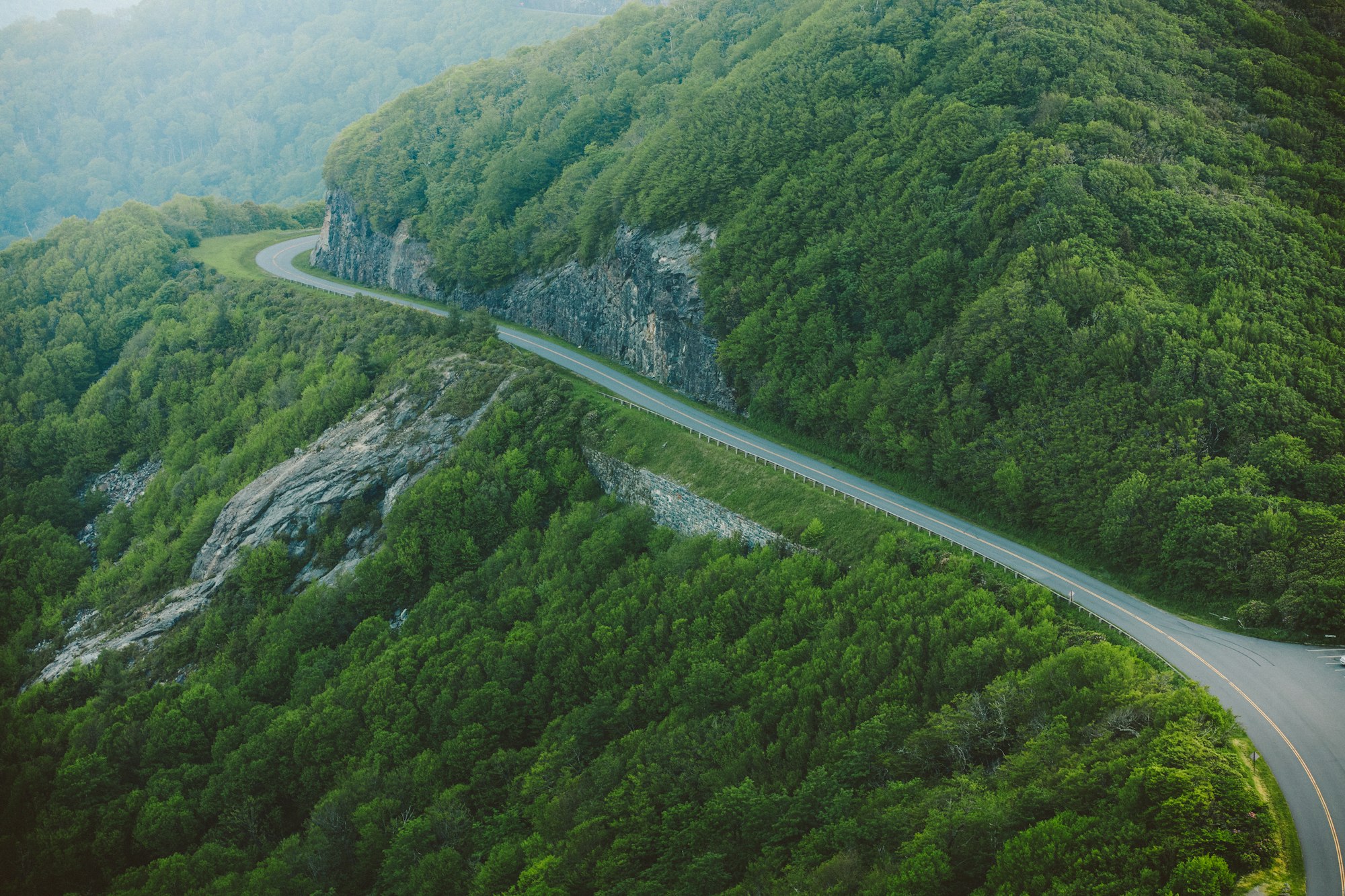 An aerial view of a winding two-lane road through forested mountains
