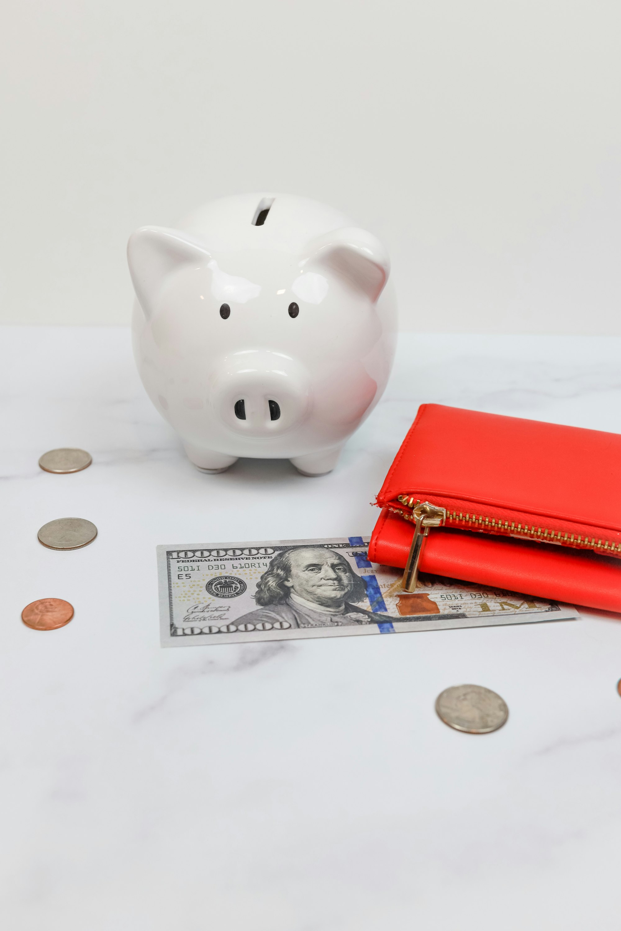 A ceramic piggy bank next to coins and a novelty bill on a marble surface