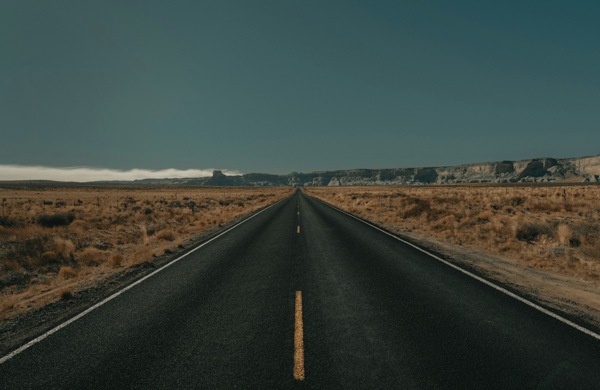 An empty two-lane highway stretching toward distant mesas under a clear sky