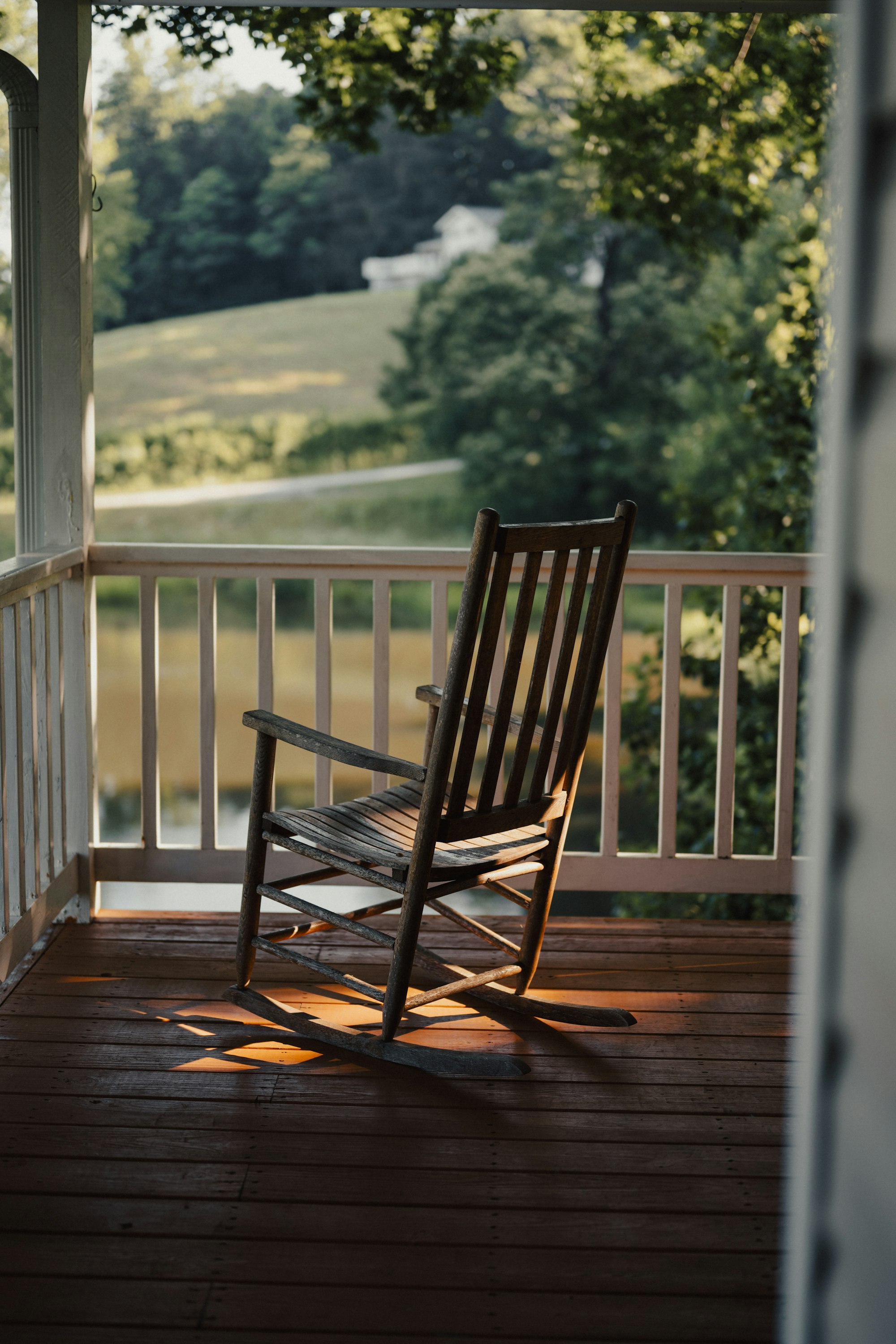 An empty wooden rocking chair on a porch overlooking a green field